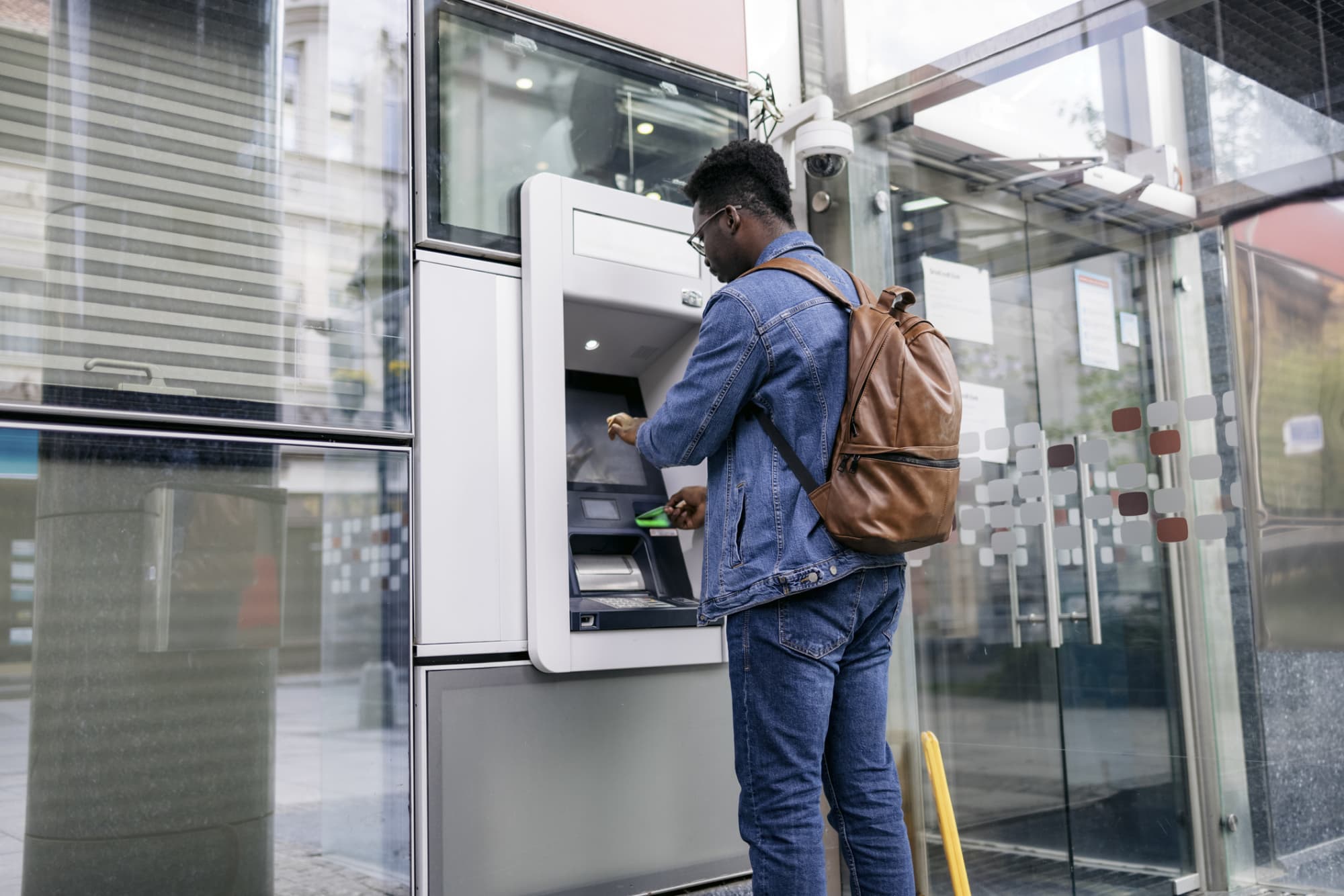 A black male college student stopping at an ATM in the city uses his debit card to retrieve cash from his bank account.