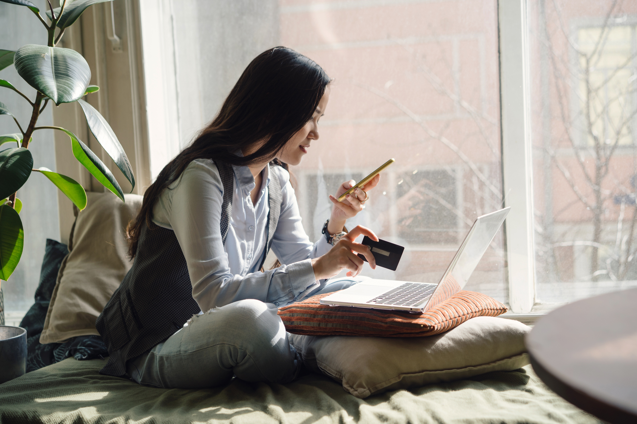 College student sitting on her bed in front of her laptop uses her credit card to pay an online bill.