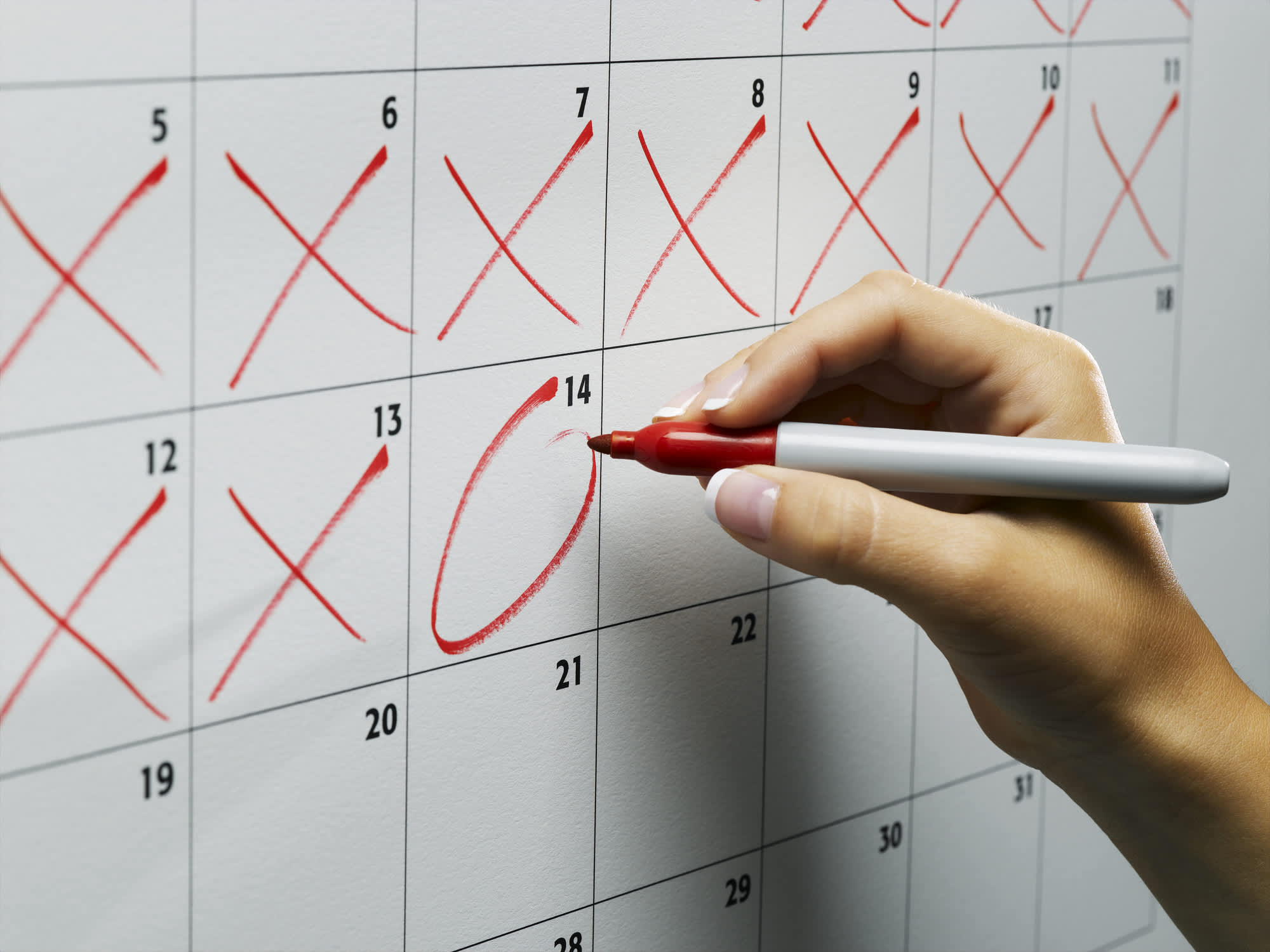 Close up of a college graduate using a red sharpie pen to mark off days on a calendar until she pays off her student loans.