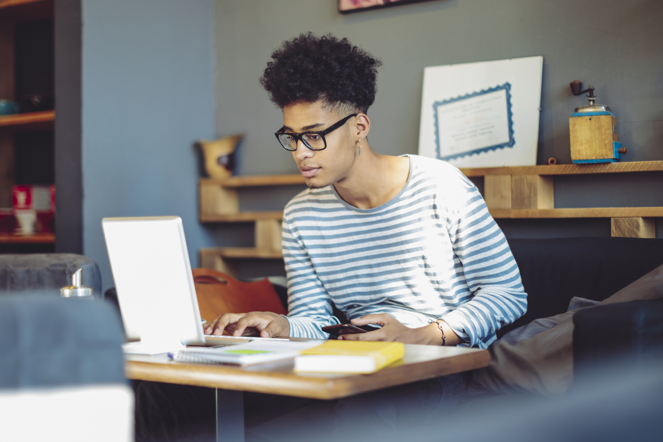 Black male student filling out the FAFSA application on his laptop computer while sitting in a cafe.