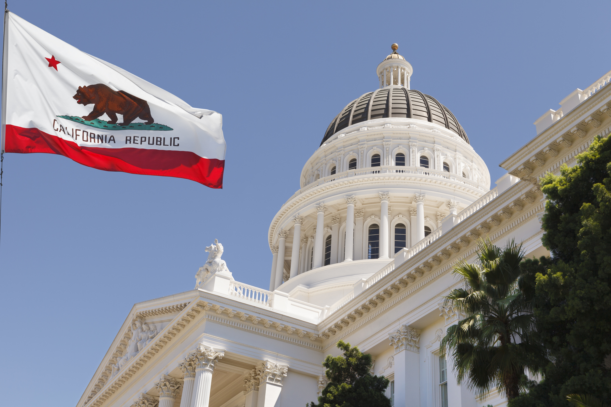 California State Capitol building with state flag in Sacramento on a windy summer day with clear sky