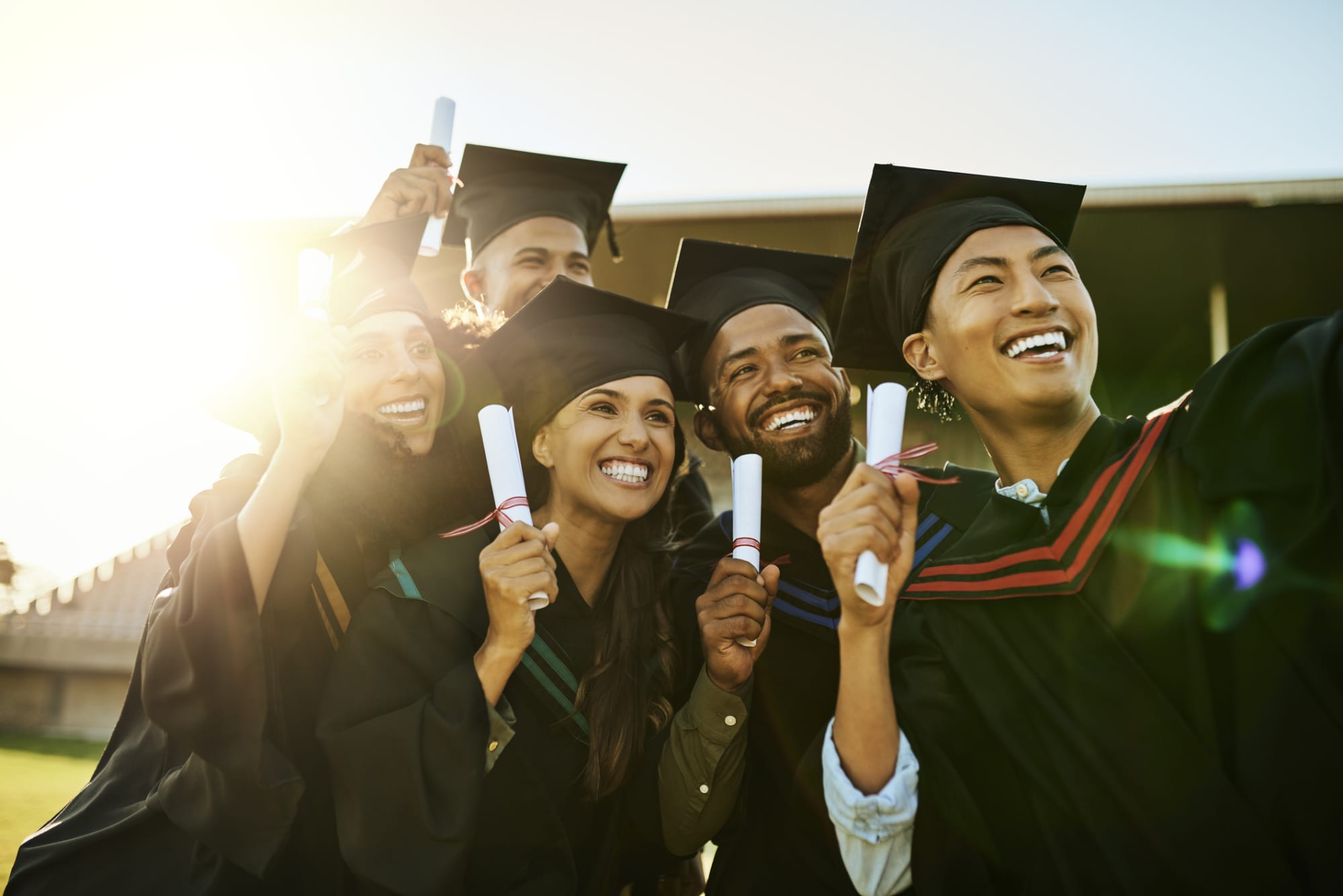 Diverse group of happy graduates in gowns taking a selfie with phone at graduation. Cheerful motivated qualified students capturing memorable photos and celebrating academic achievement and milestone