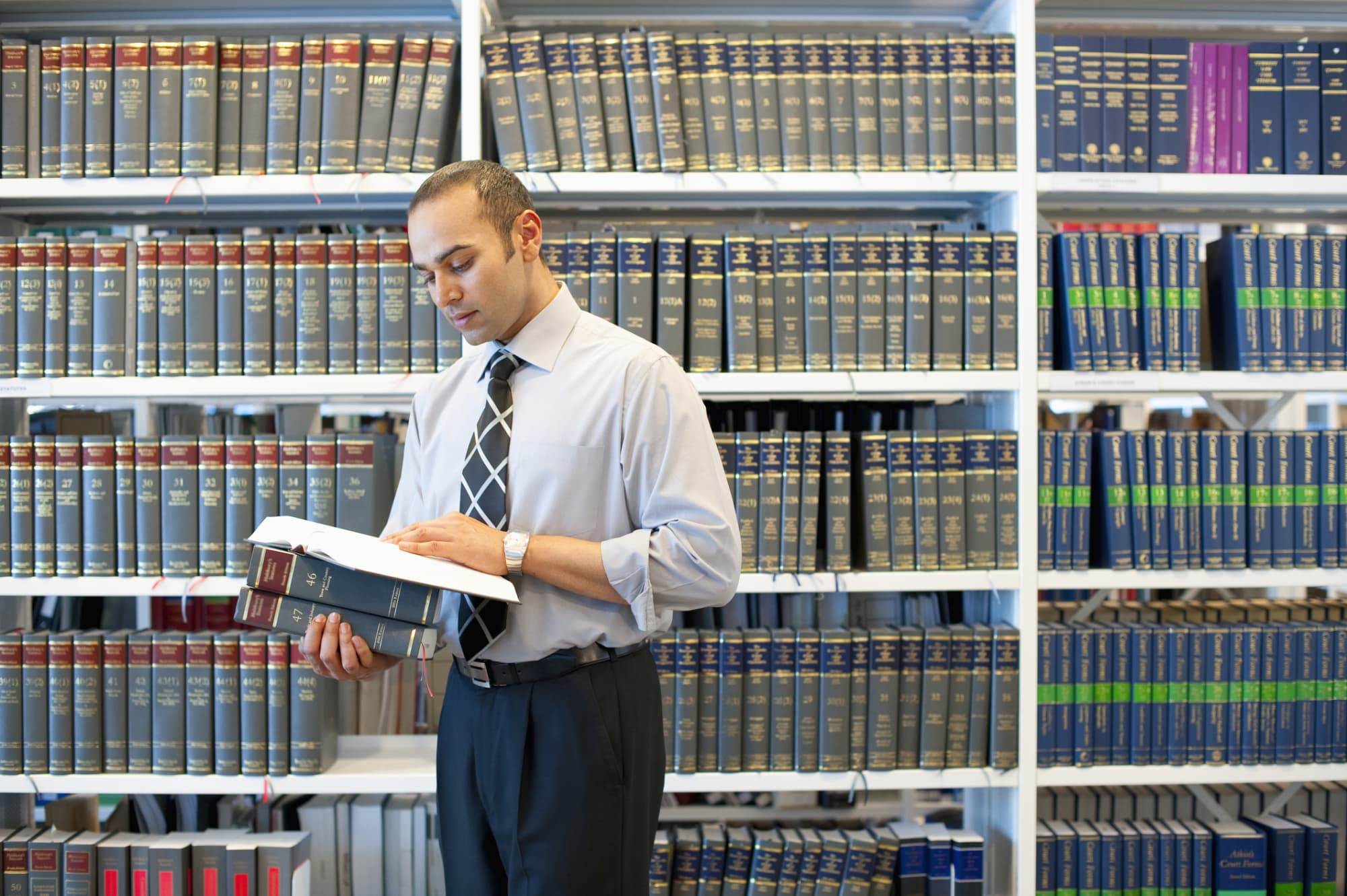 South Asian male law student reading a legal textbook in the library stacks on campus.