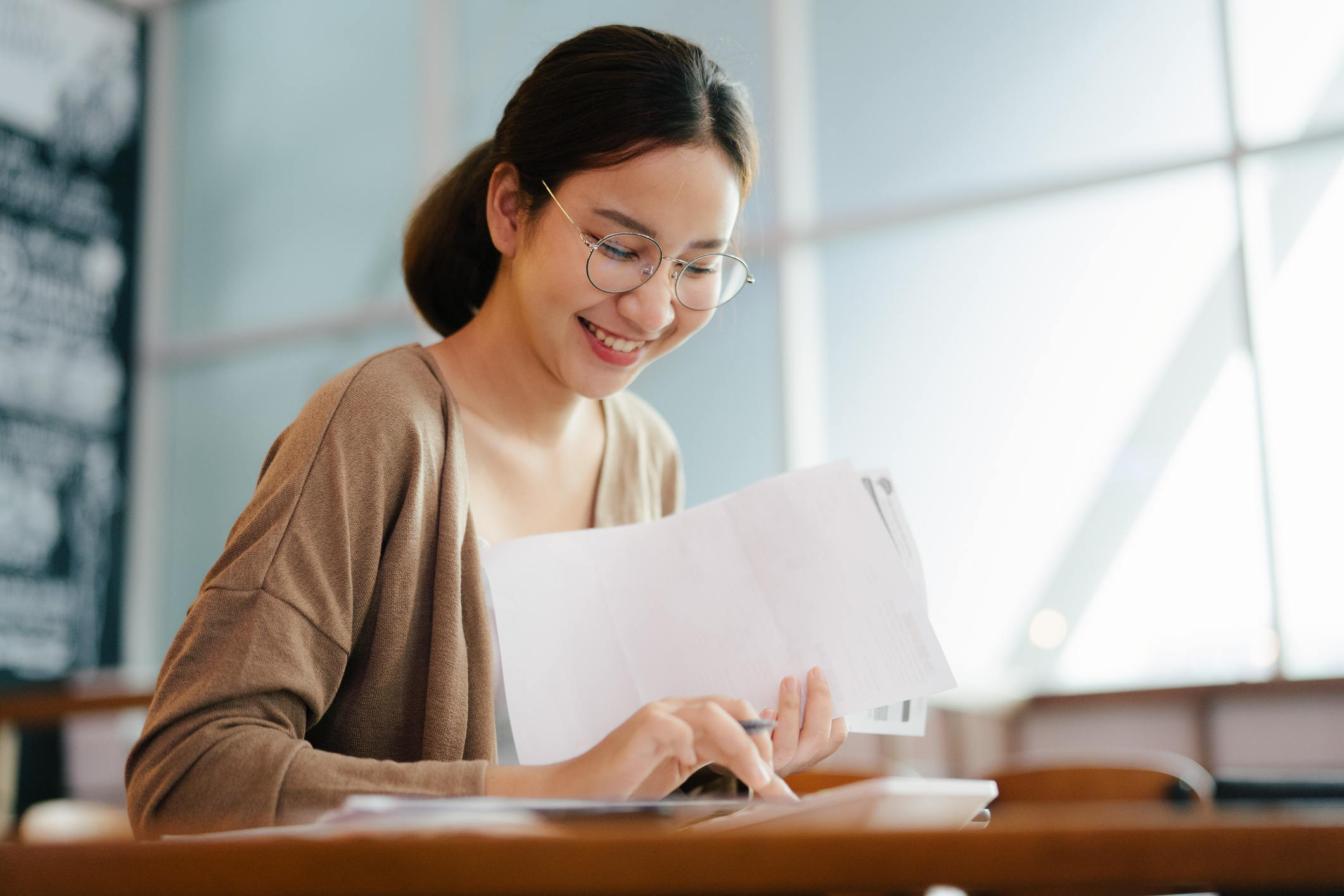 Asian American female college student uses a calculator to review her college savings plan documents and progress.