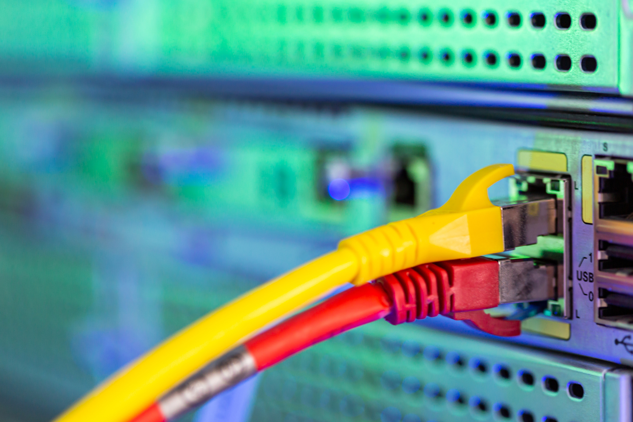 Close-up on the pair of yellow and red Ethernet cables plugged in the panel of telecommunication server. Selective focus shot with blurred background copy space