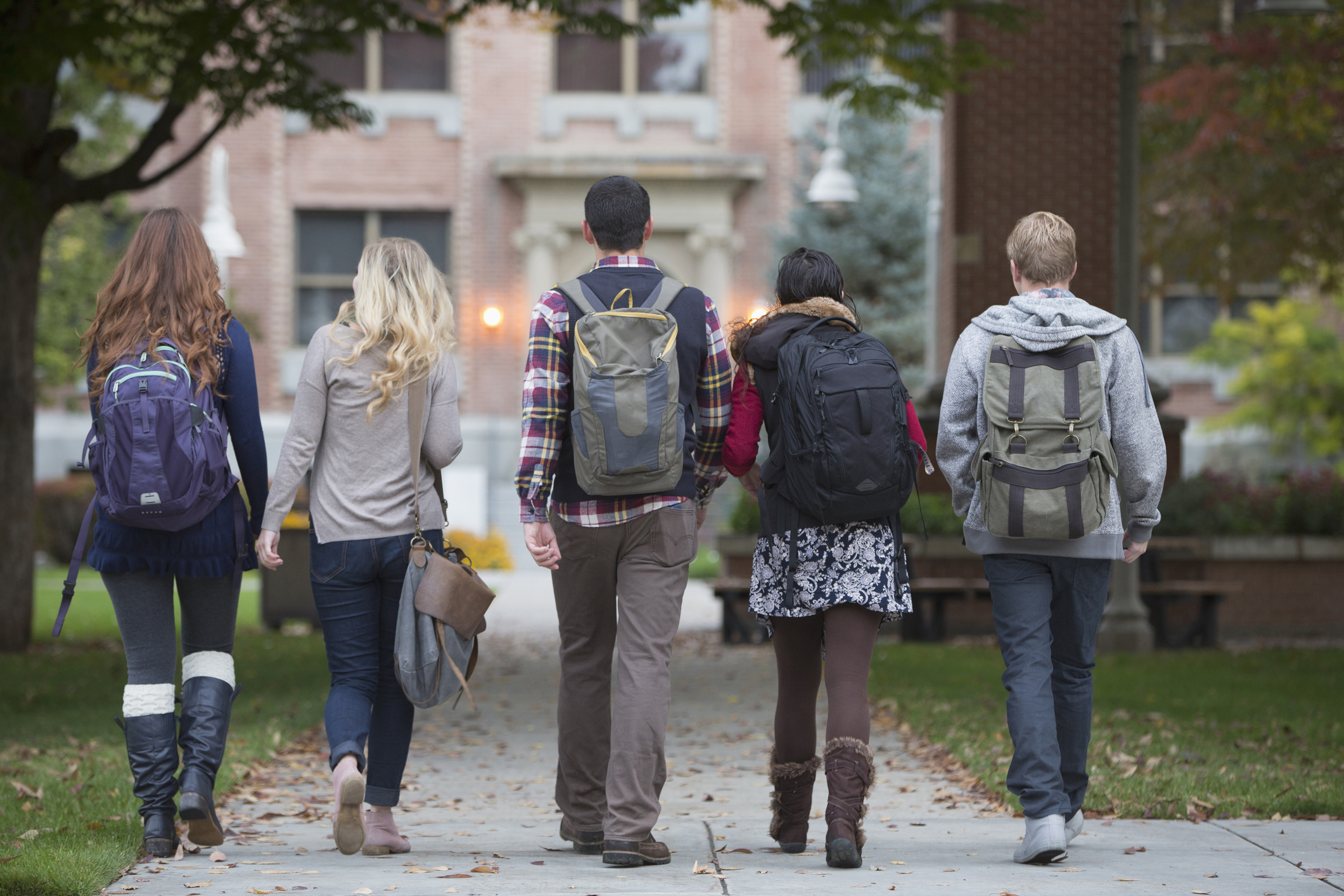 A group of 5 college students walk to class together on campus.