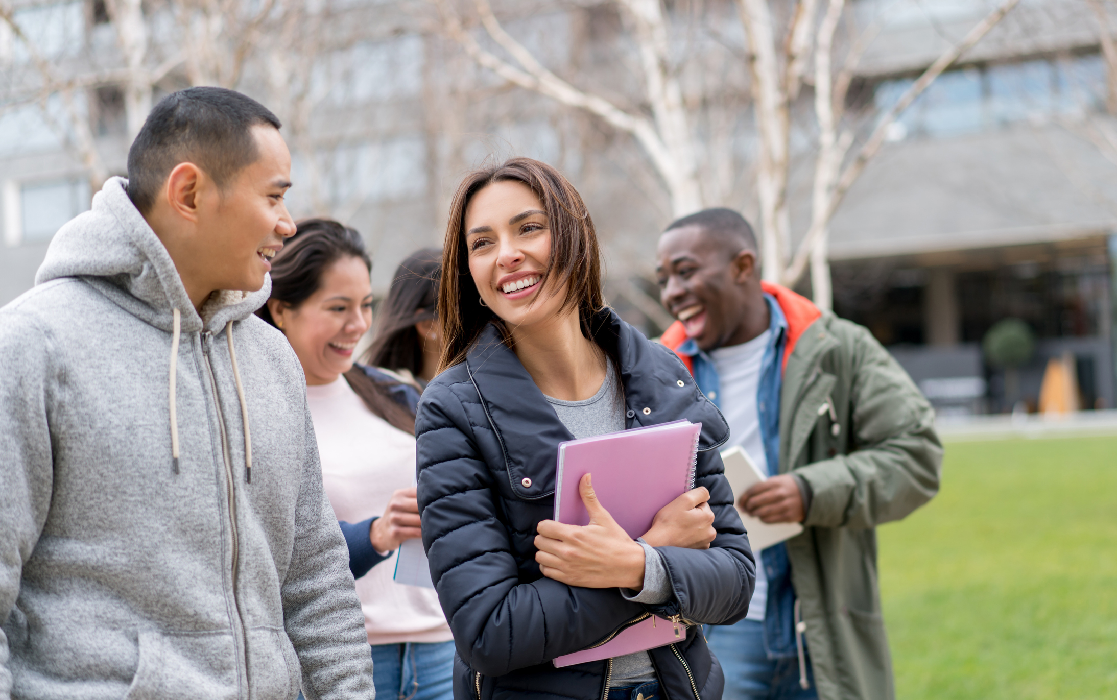 A small group of multi-ethnic international college students walking outside on campus. They are chatting and laughing together on their way to class.