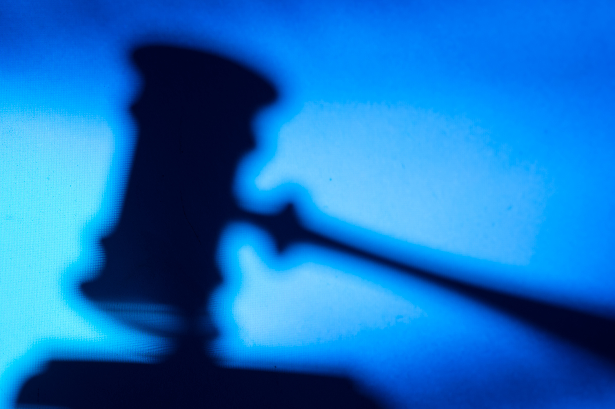 A faded silhouette of a judge's gavel resting on a bench in a courthouse.