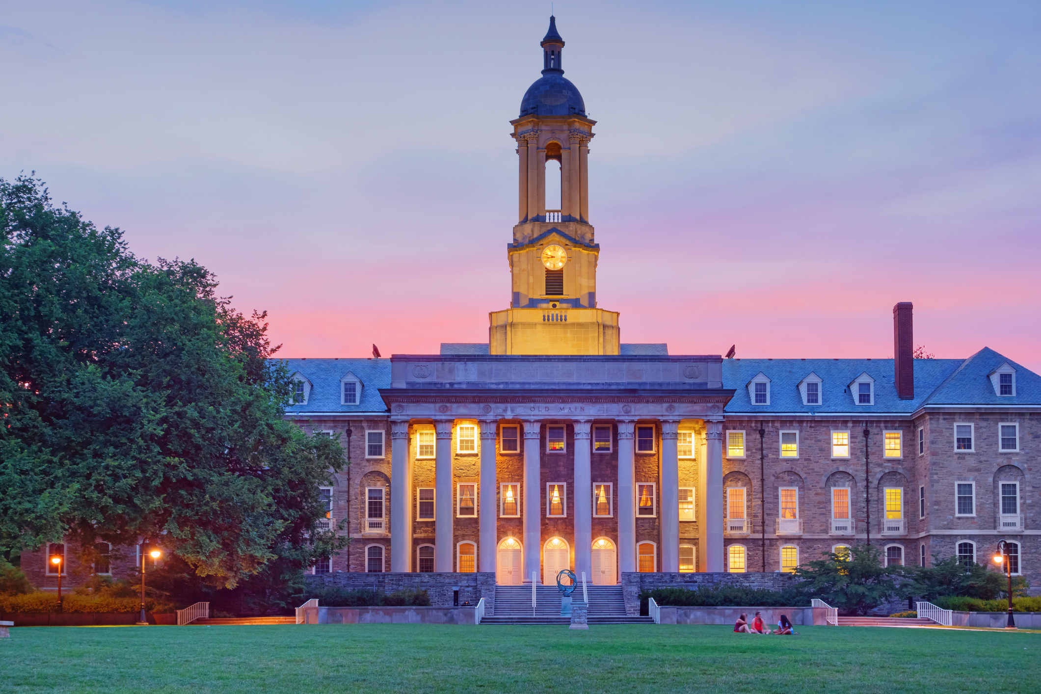 Students chat in front of Old Main, the main administrative building of Penn State after sunset. It is located at University Park in State College, Pennsylvania, USA. Pennsylvania State University (commonly referred to as Penn State or PSU) is a public university with campuses and facilities throughout Pennsylvania.