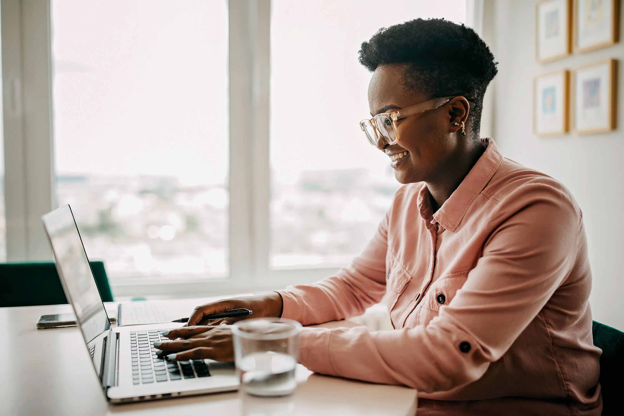 A woman working from home on her laptop. She is sitting at her desk by a big bright window.