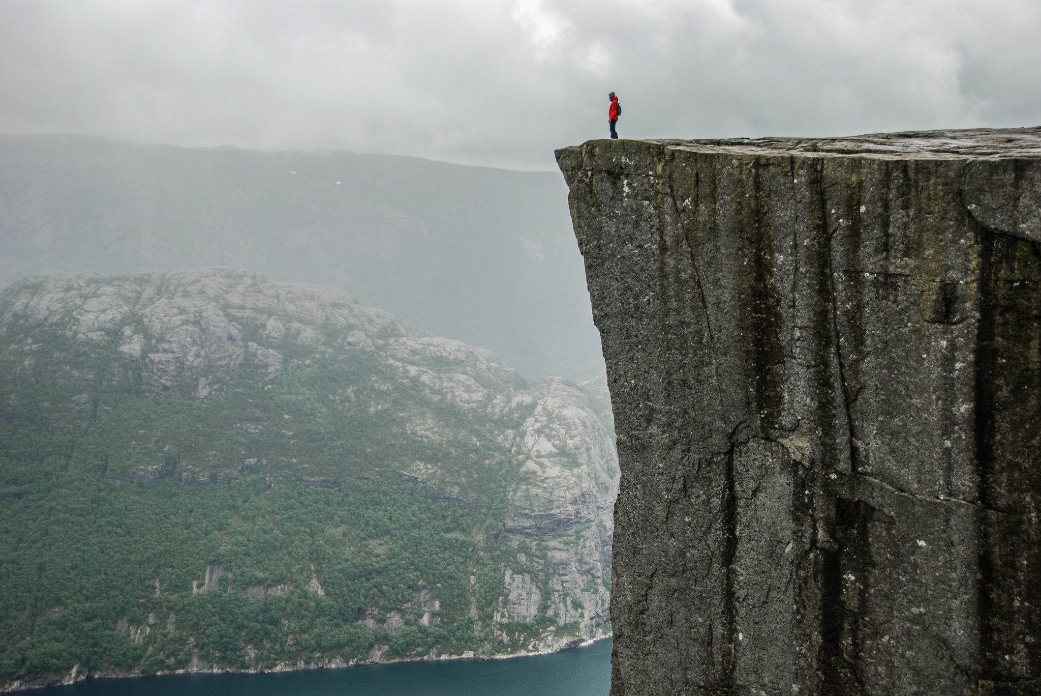 A picture of a person standing at the edge of a very large cliff looking out around them.