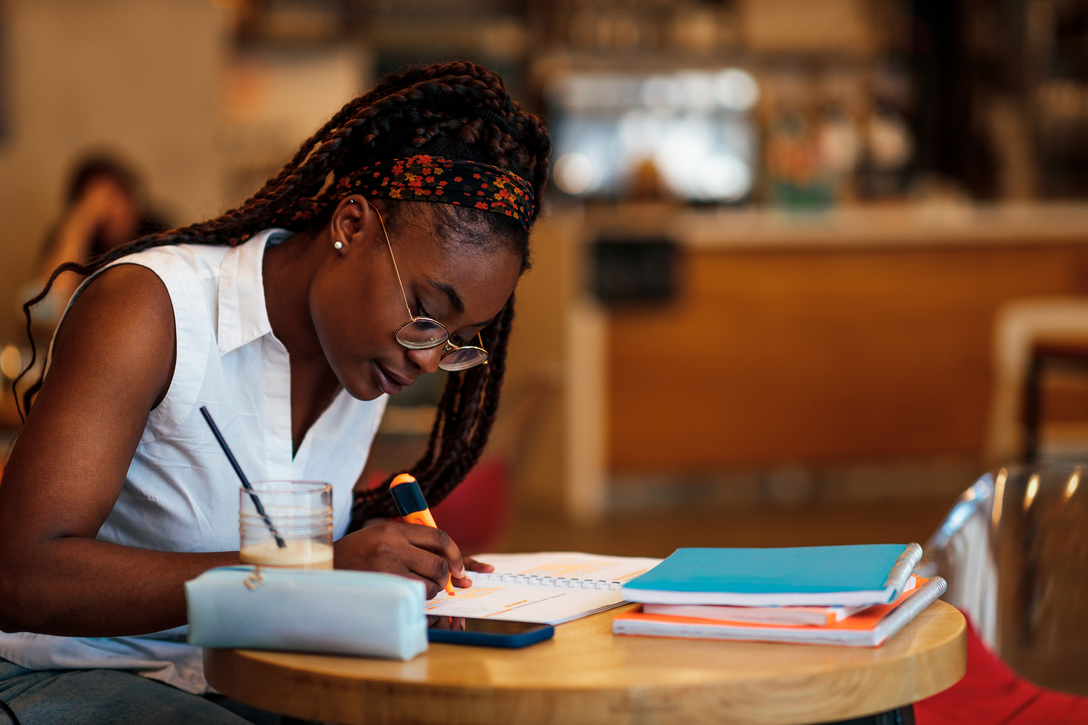 Black female student taking notes while studying for her MCAT exam at a cafe.