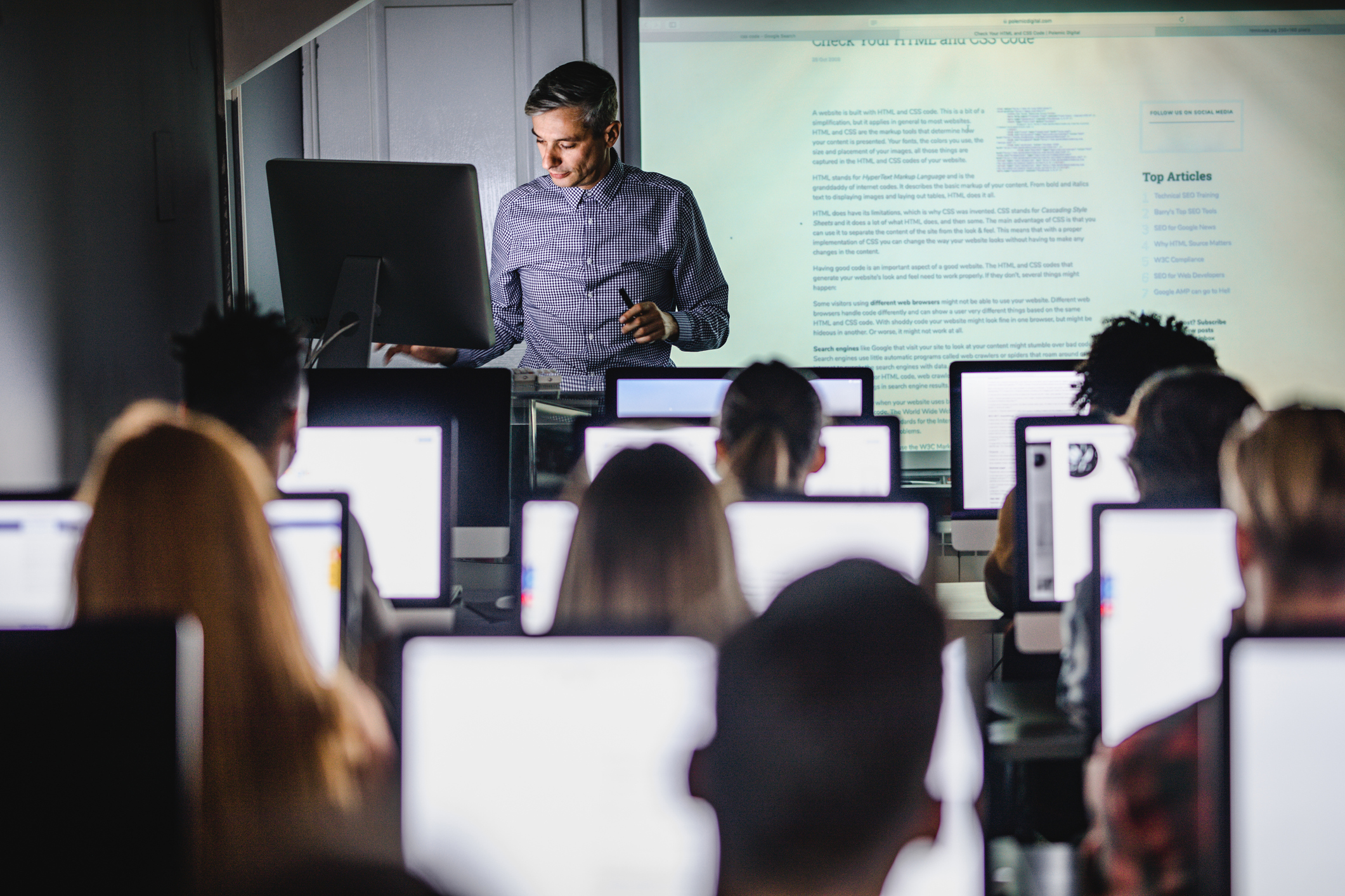 Male teacher giving a lecture from desktop PC during a class at computer lab.