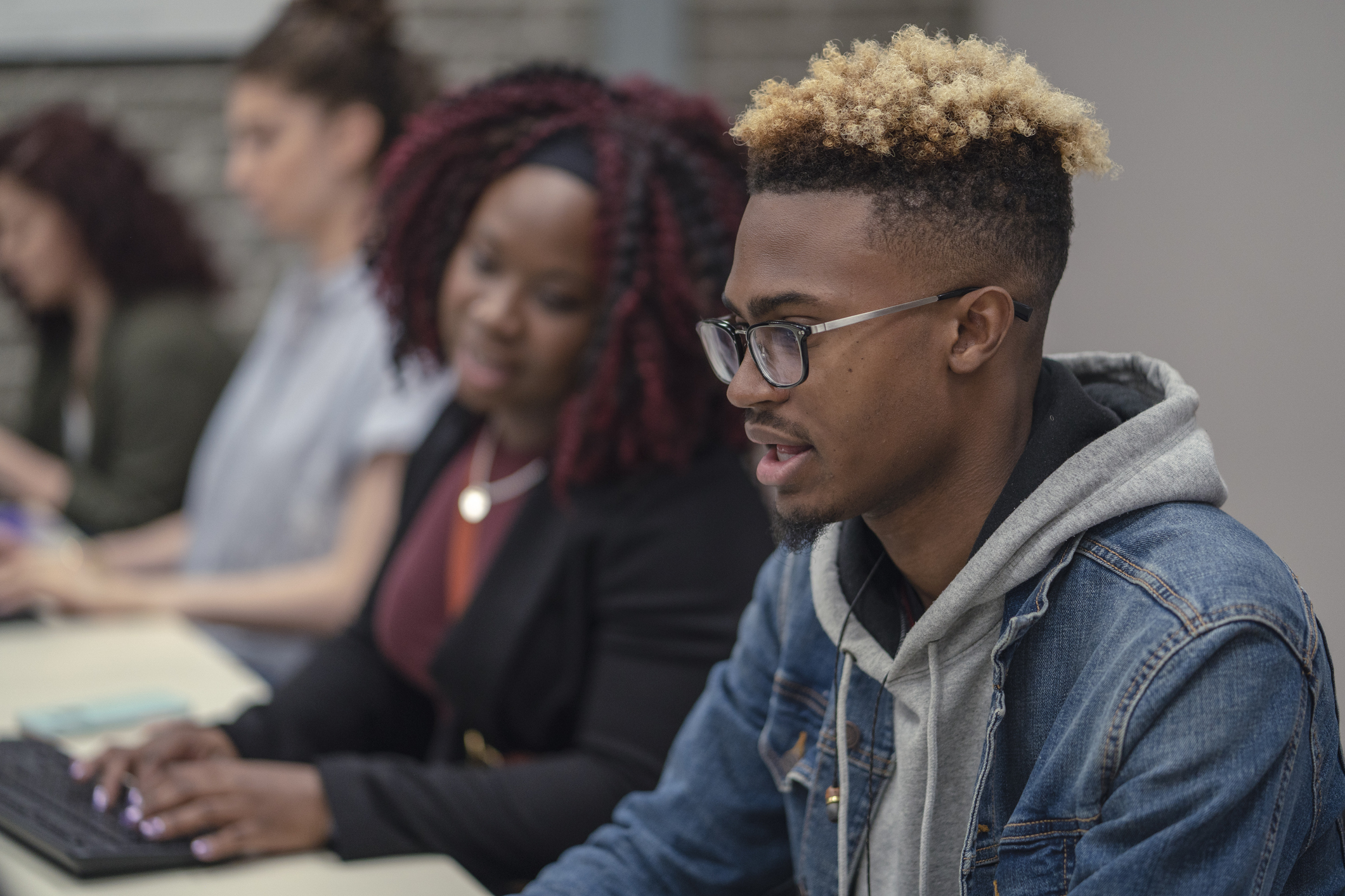 A multi-ethnic group of students are working together on a university assignment. They are researching and collaborating as a team. They are typing on computers and taking notes. They are wearing casual clothes. The room is located on the university campus.