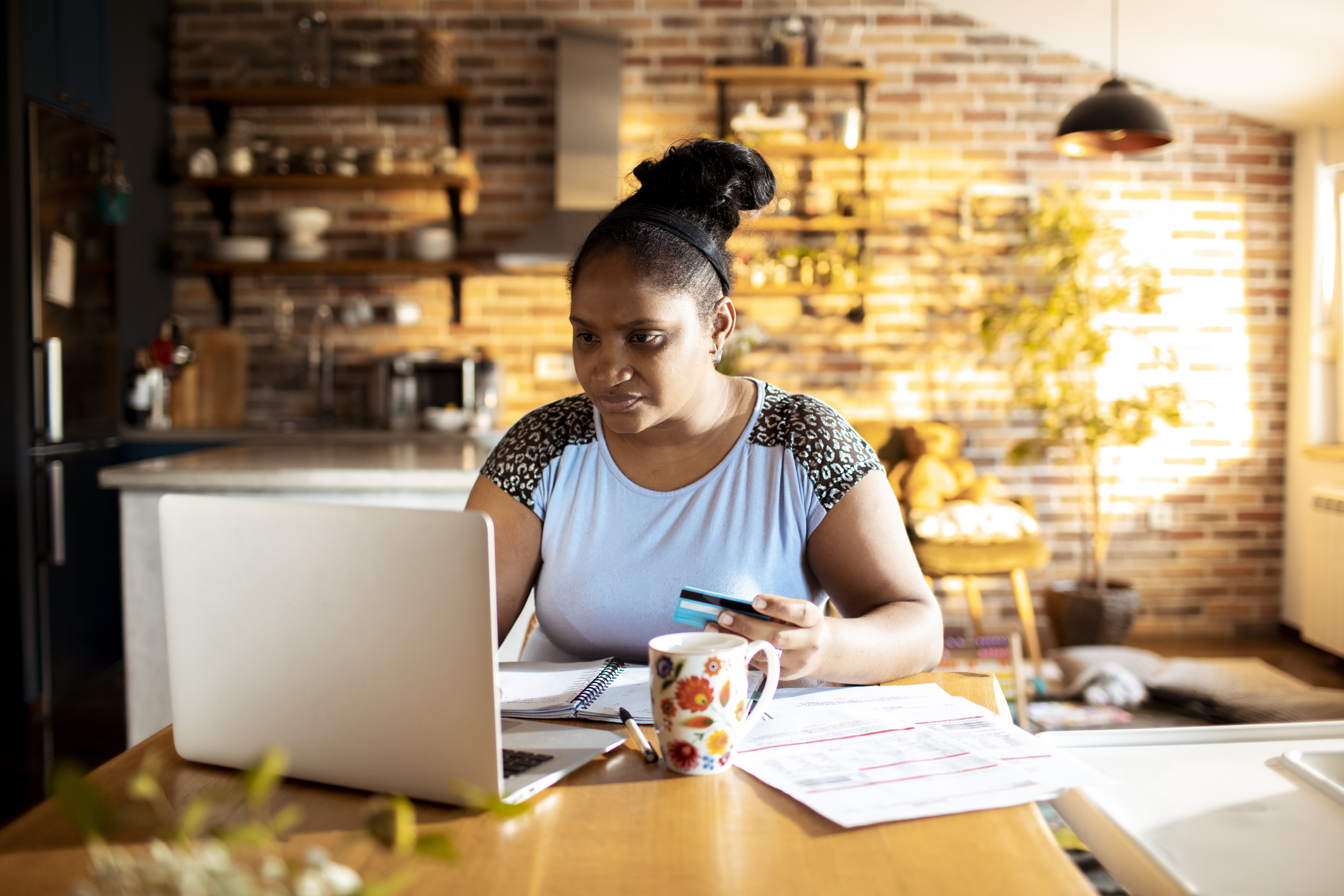 Female college student sitting at her dining room table in her apartment. She is using her credit card to make a tuition payment on her laptop computer.