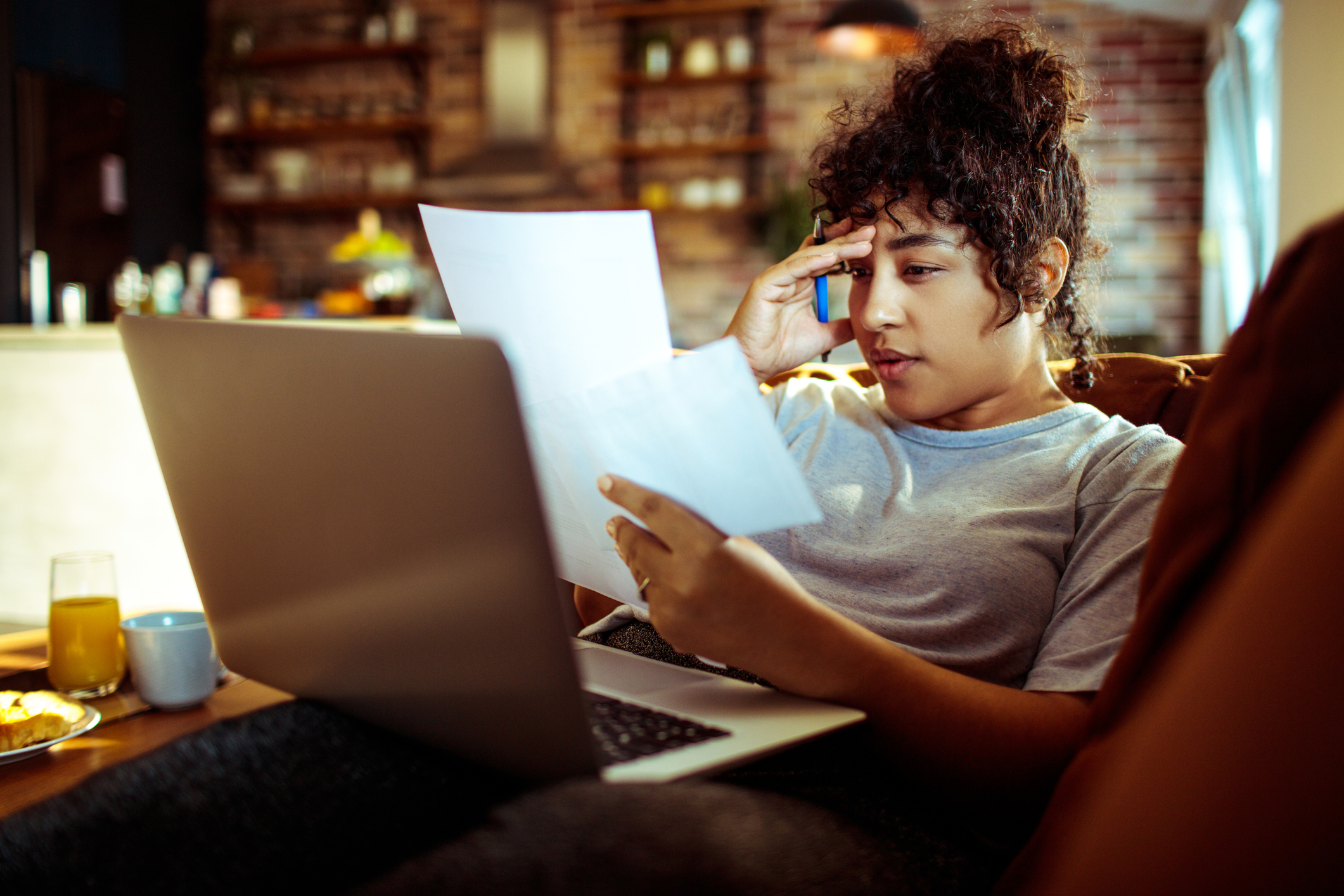 Woman sitting on her living room couch at home. She is using her laptop while paying off student loan bills.