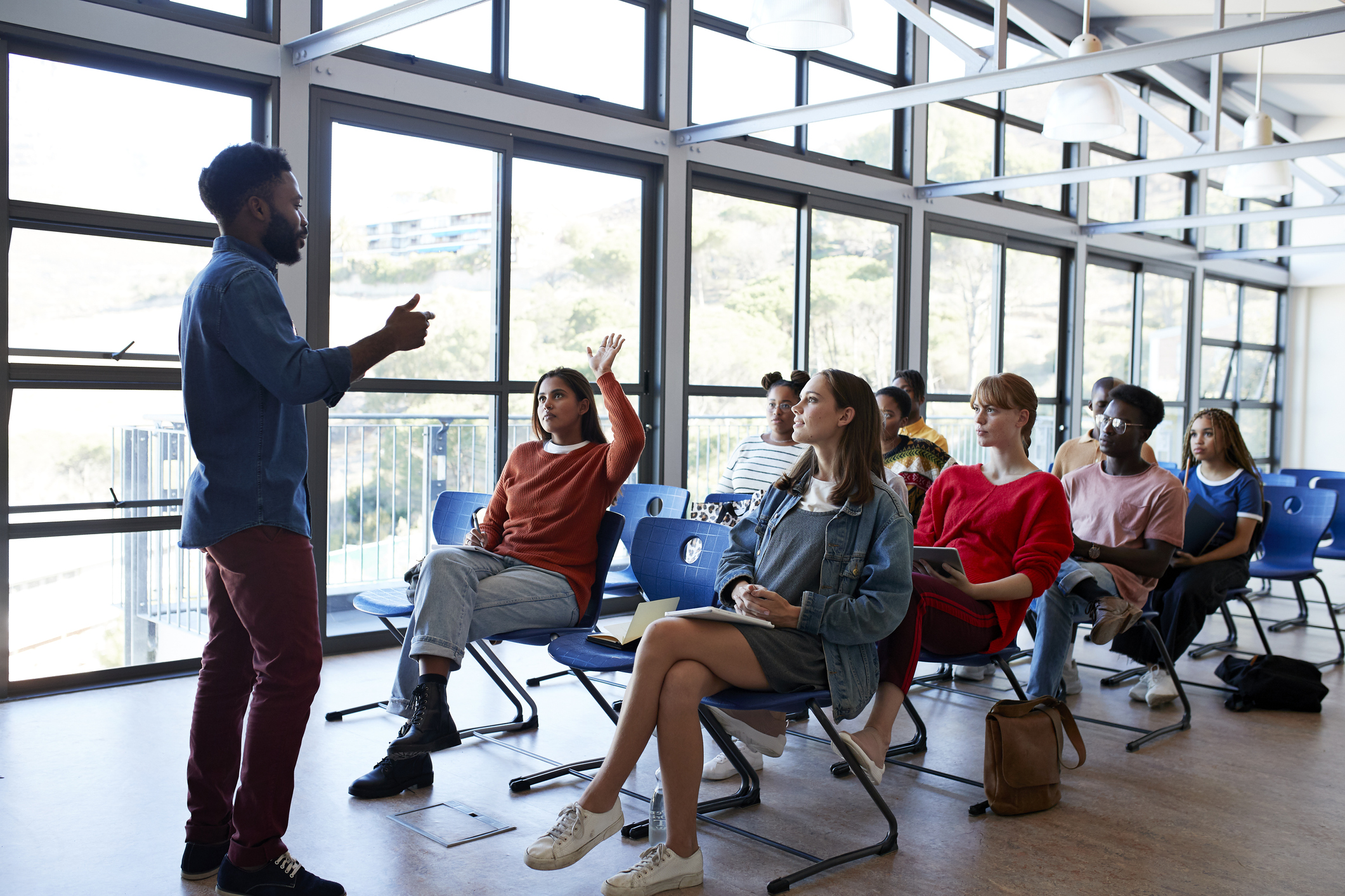 Young male professor explaining multi-ethnic students sitting on chairs by window in classroom at university