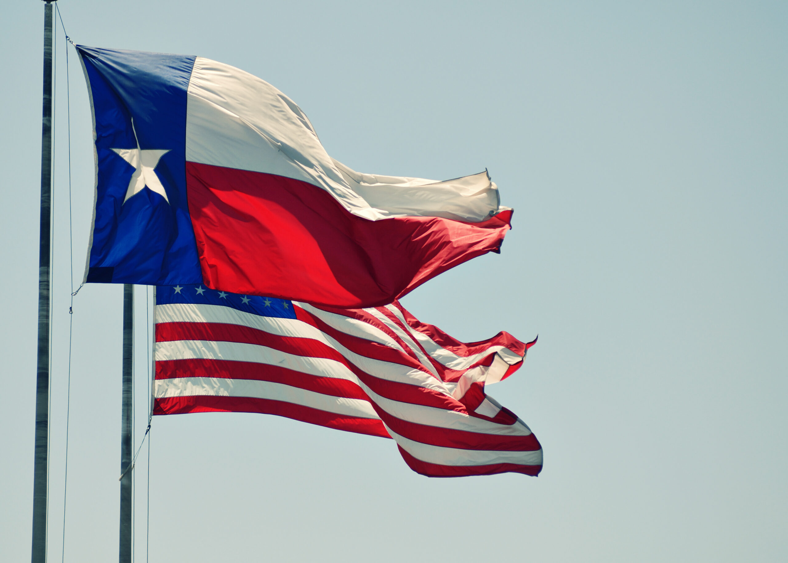 The Texas state flag and the USA flag blowing in the wind side by side.