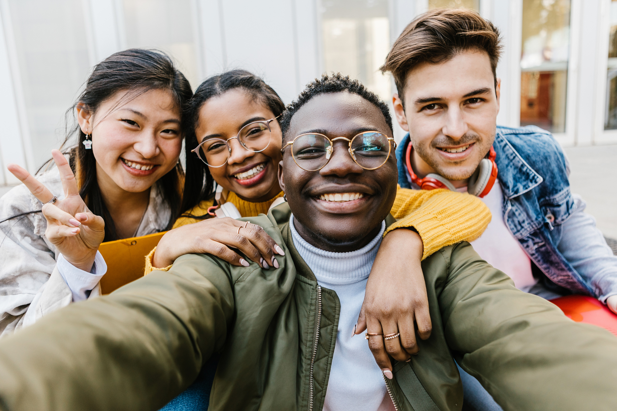 A diverse group of college student friends after class. They are hugging each other and smiling while taking selfie photos.