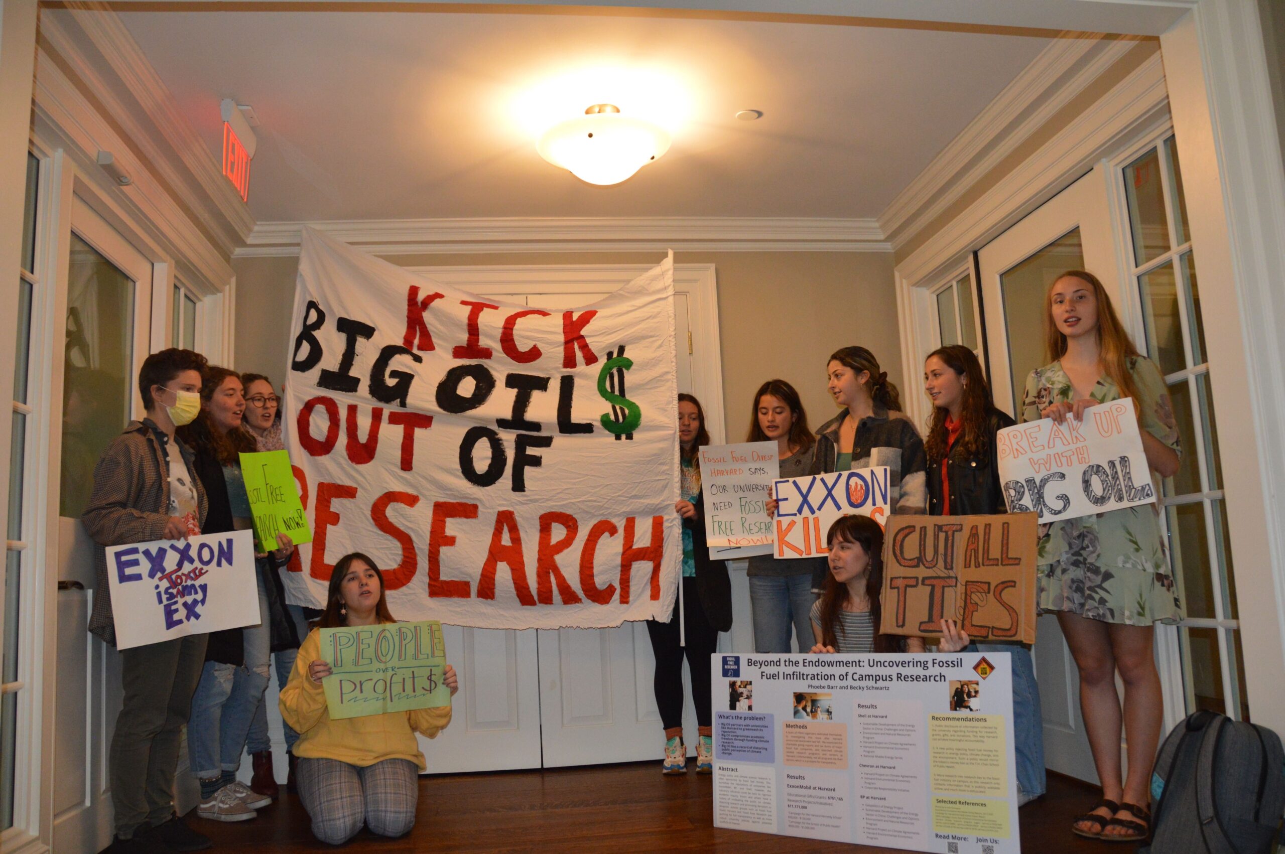 A group of college students standing in a living room holding protest signs related to getting rid of big oil.