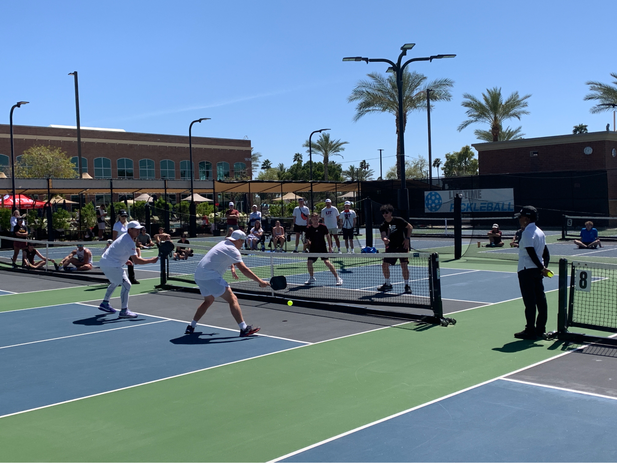 A group of people wearing white clothing playing pickleball on a bright sunny day.