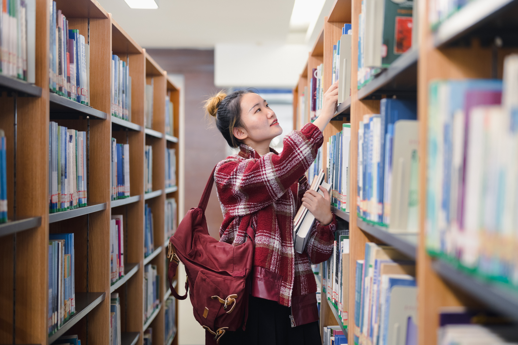 Female Asian American college student looking for textbooks on the shelves in her university's library.