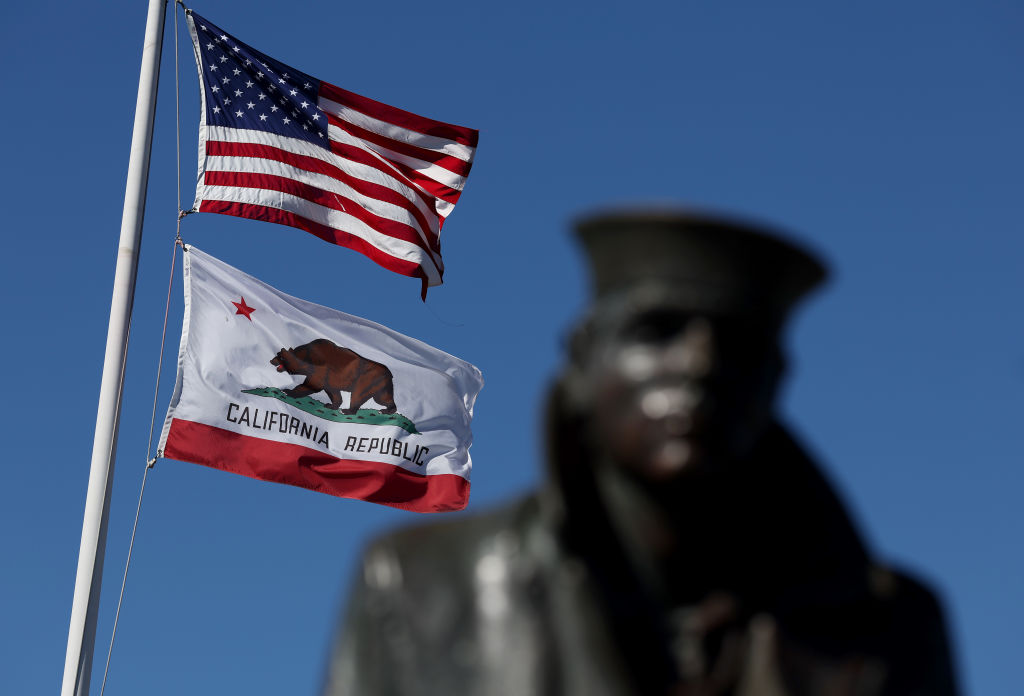 An American flag and the California State flag flying next to the Lone Sailor statue in Sausalito, California.