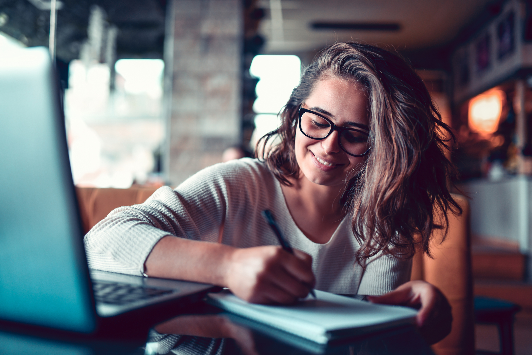 Female Taking Notes For Work Project While Researching Topic On Laptop