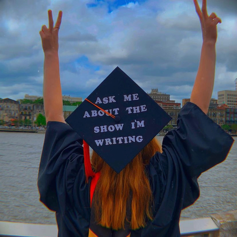 Alexis Rausch, a 2023 graduate from the Savannah College of Art and Design in Georgia, at her graduation ceremony. She is wearing a cap decorated with the words, "Ask me about the show I'm writing."