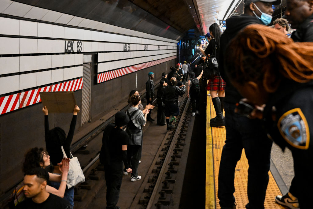 Protesters stand on the trains tracks at the Lexington Ave/63rd Street subway station as a train approaches the station