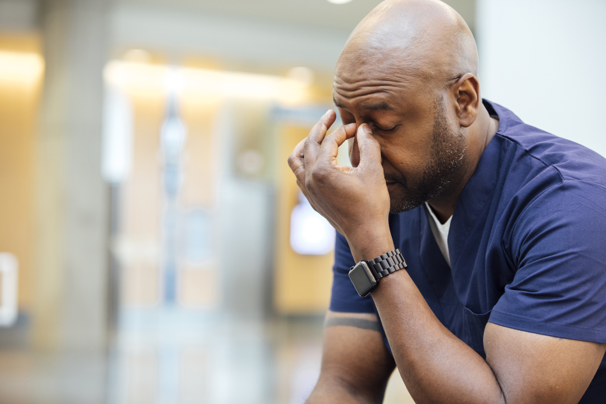 Tired Black male nurse sitting in a chair in the hospital break room. He is rubbing his temples.