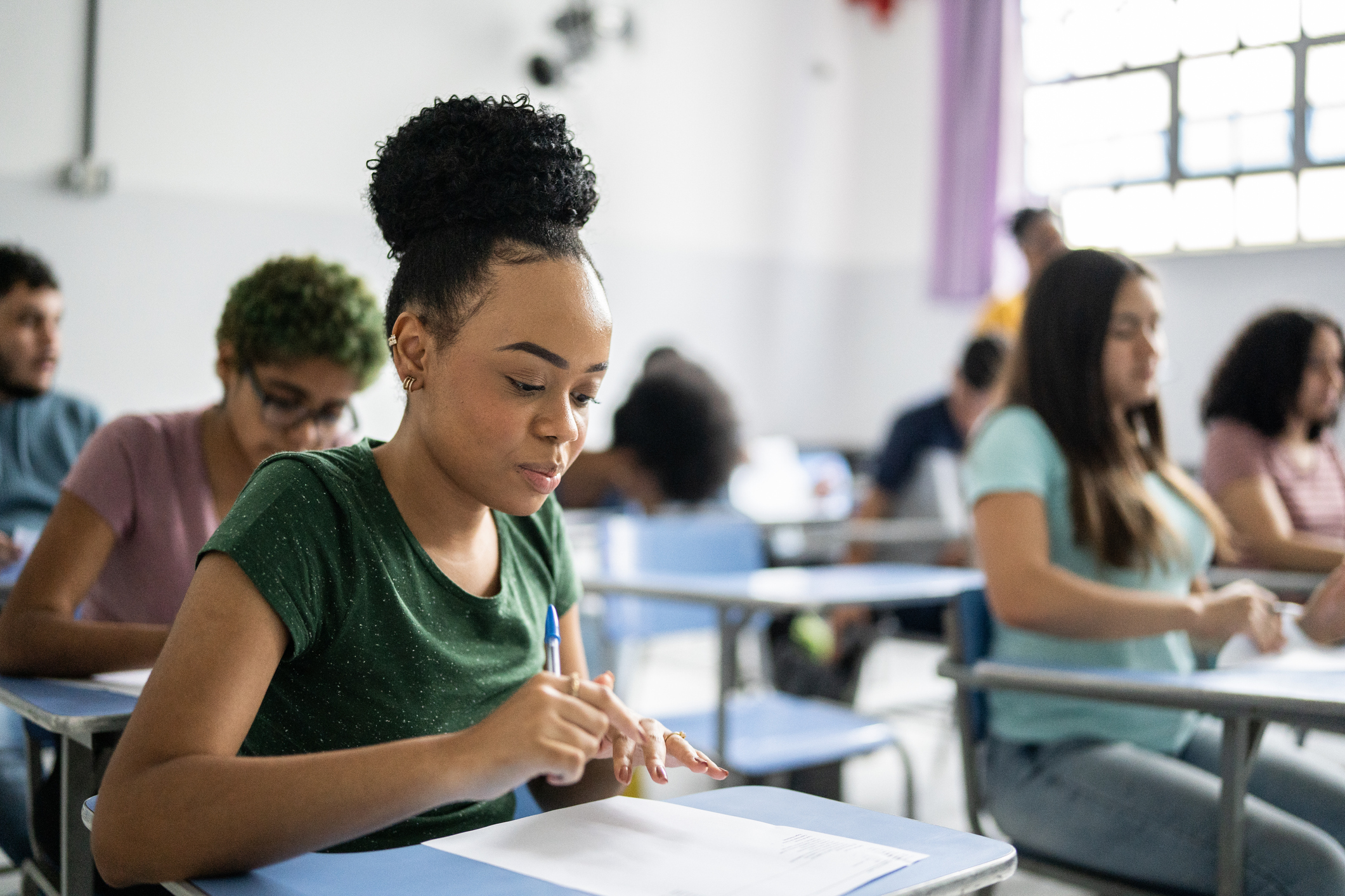 High school student taking an exam in a classroom full of other students.