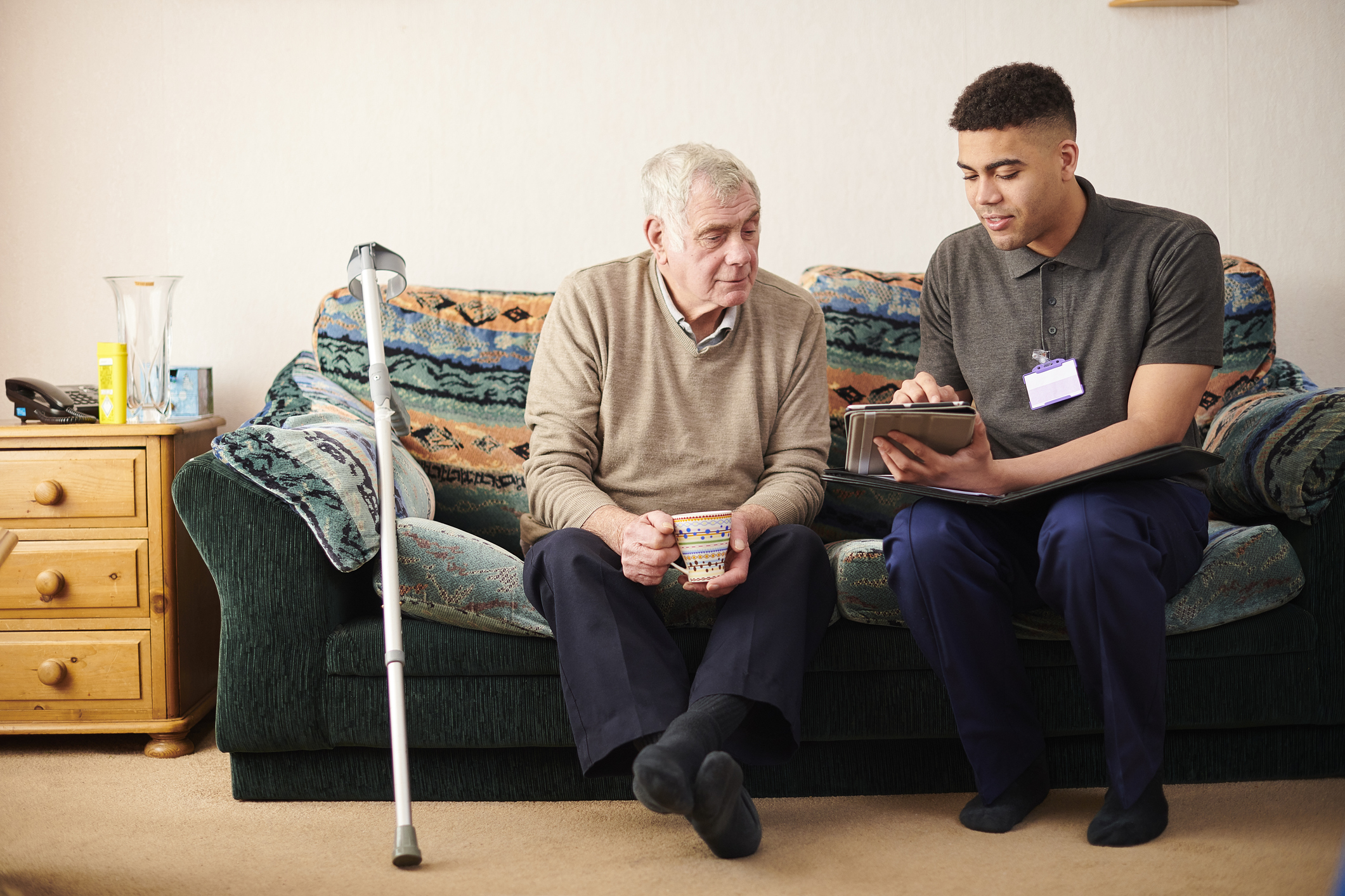 Black male social worker paying a house visit to a senior male client. They are sitting on the client's couch in his living room and chatting together.