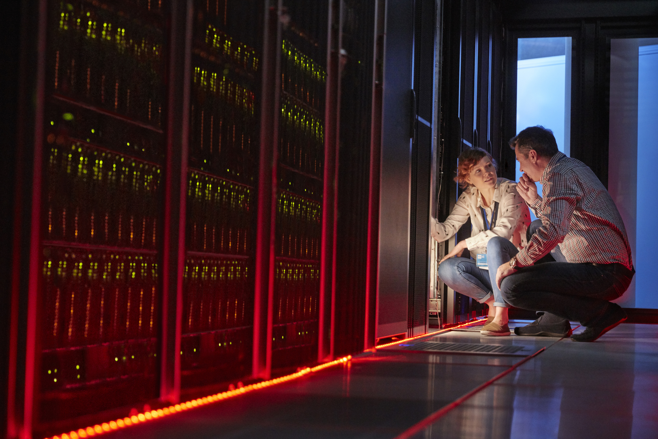 IT technicians talking at glowing panel in dark server room