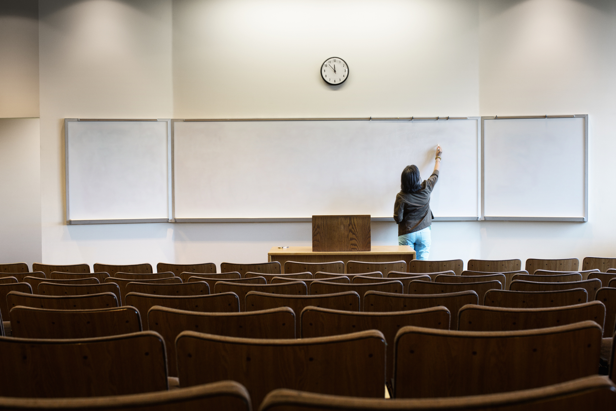 Female professor writing on whiteboard in an empty university lecture hall before class begins.