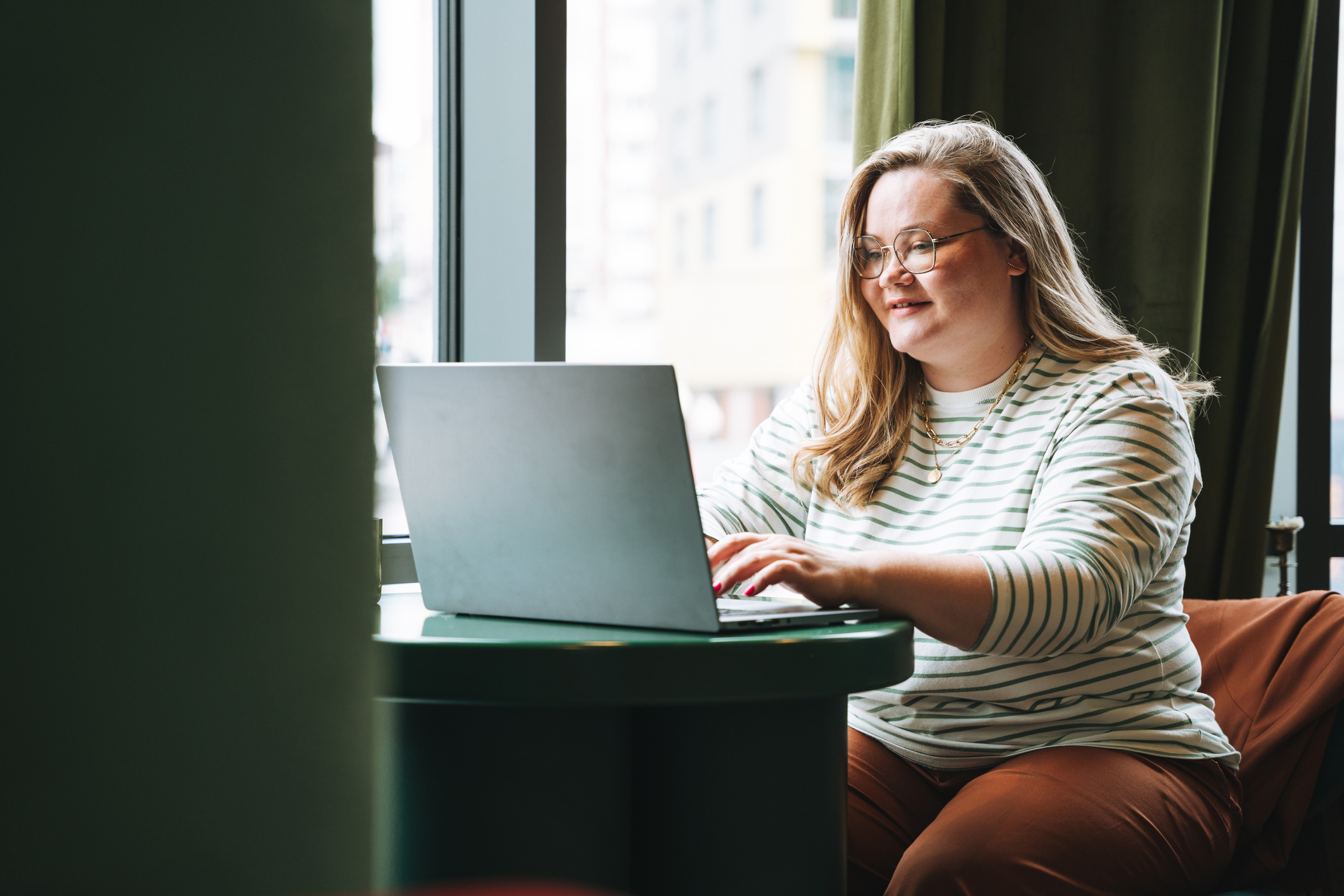 Caucasian female college student in casual clothes working on her laptop in a cafe.
