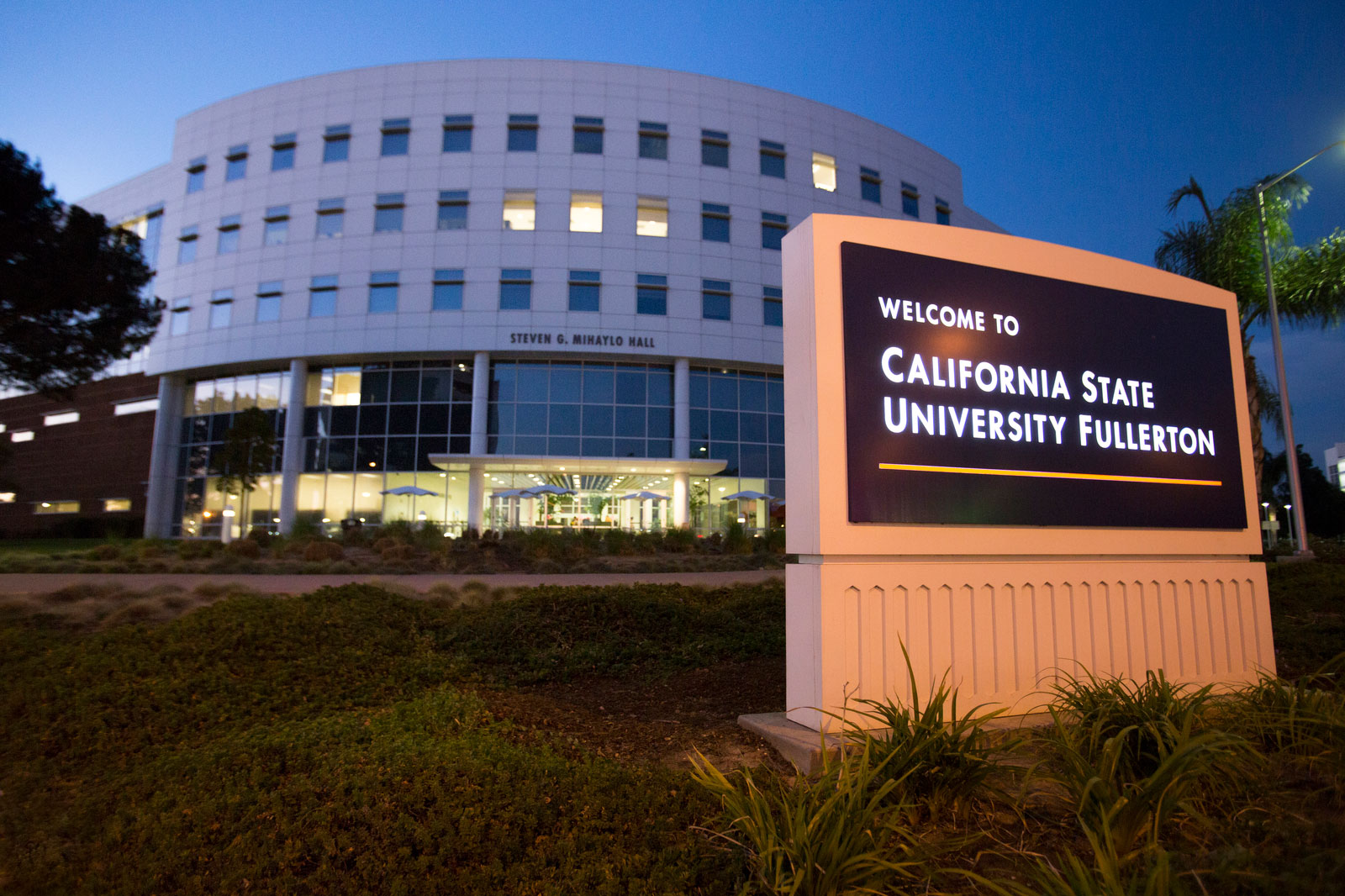 Campus sign for California State University Fullerton and building at dusk